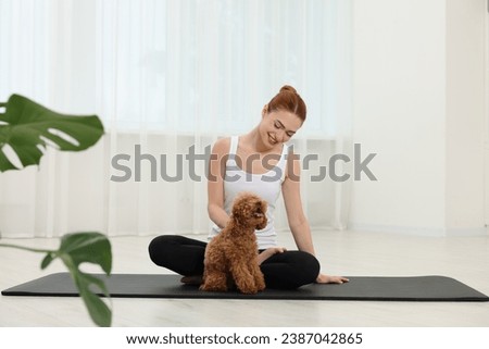 Happy young woman practicing yoga on mat with her cute dog indoors