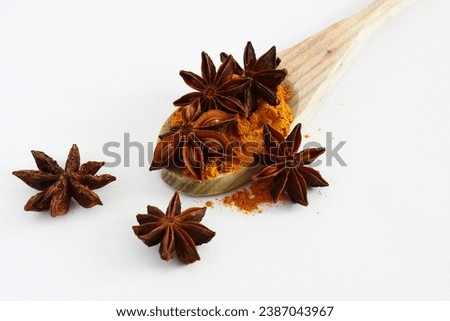 close up of a cooking wood spoon with spices anise and turmeric powder on a white background