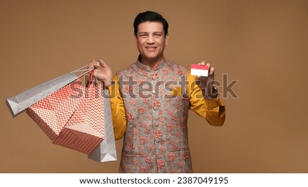 Portraits of young Indian man holding shopping bags and showing credit card