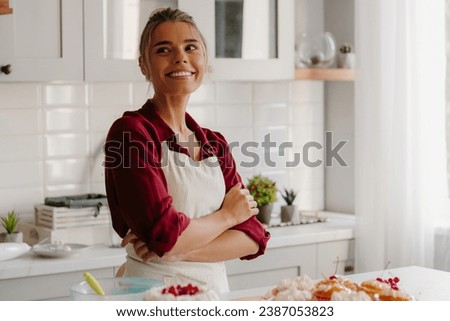 Joyful young female confectioner looking thoughtful while making cakes and muffins on the kitchen