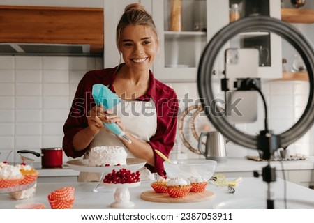 Confident female baker applying whipped cream on cake while streaming online from the kitchen