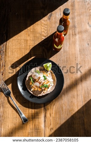 Overhead of a crispy fish taco on dark plate with sauce drizzle and beer with a sliced lime, hot sauces, and a silver fork in the background.
