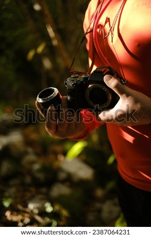 Photographer switch lens outdoor during his Journey in the Woods wearing orange technical shirt