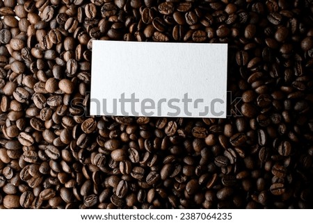 Freshly roasted fragnant coffee beans background with business card above, close up view. Coffee beans background. Background of roasted coffee beans