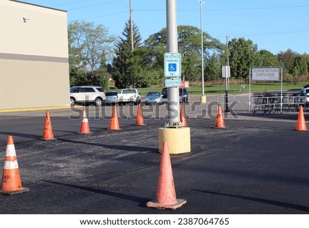 A handicap parking space sign sits blocked off in a parking lot by orange cones