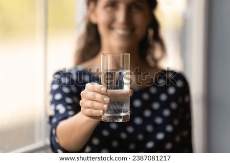 Close up focus on glass of pure filtered mineral water in happy woman hand, offering to camera, satisfied young female recommending healthy lifestyle habit, natural beauty concept, body refreshment