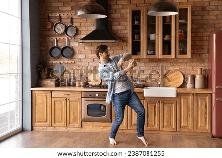 Funny carefree young man dancing, moving to favorite music in cozy kitchen at home alone, active excited male having fun, celebrating relocation into first own apartment, enjoying leisure time Royalty-Free Stock Photo #2387081255