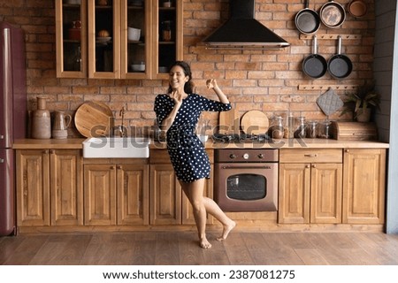 Full length happy young woman dancing in kitchen at home, having fun, moving to favorite music alone, smiling attractive female enjoying leisure time, excited by relocation in first own apartment Royalty-Free Stock Photo #2387081275