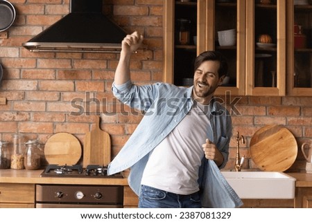 Overjoyed carefree man dancing, moving to favorite music in cozy kitchen at home, active excited male having fun alone, celebrating relocation into first own apartment, enjoying leisure time Royalty-Free Stock Photo #2387081329