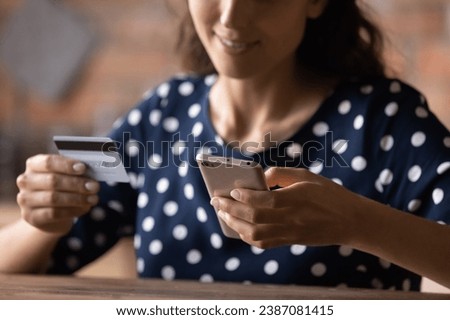 Close up cropped of woman holding credit card and smartphone, smiling young female paying online, using banking service, entering information, shopping, ordering in store, doing secure payment