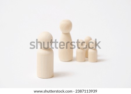 The wooden father doll stands apart from wooden mother doll with children in white background