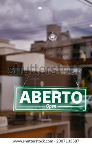Bilingual sign with the words Aberto and Open in Portuguese and English on the glass door of a store in Brazil