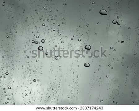 It is a photograph of rain drops falling on clear glass, creating a beautiful reflection.