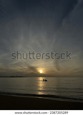 a picture of sea, with sunrise and 2 fishman in the middle
