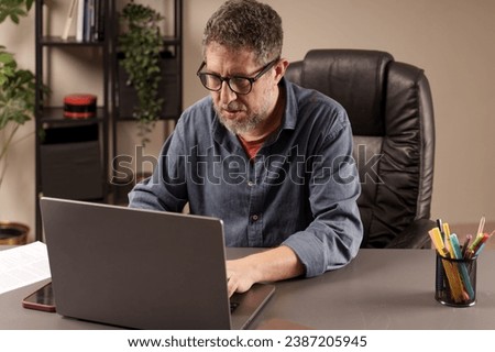 Concentrated man working diligently on his laptop in a home office environment, exemplifying remote work professionalism. Royalty-Free Stock Photo #2387205945