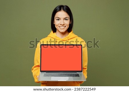 Young IT Latin woman wears yellow hoody casual clothes hold use work on laptop pc computer with blank screen workspace area isolated on plain pastel green background studio portrait. Lifestyle concept