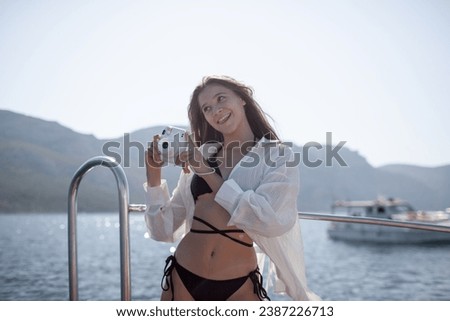 A beautiful young girl with a slender figure travels and rests on a boat during a summer vacation in the open sea or ocean against the background of the island.Female makes photo on camera