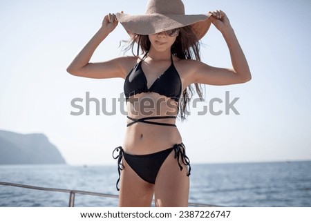 A beautiful young girl with a slender figure travels and rests on a boat during a summer vacation in the open sea or ocean against the background of the island. A model is wearing a black swimsuit