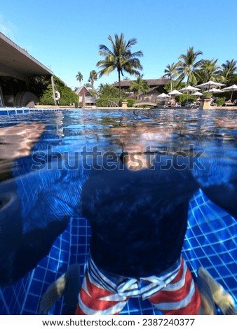 Underwater photo of a sportive young male boy who is swimming anf having fun in a deep blue swimming pool alone with no people around during his relaxing holidays. He has the pool jus for himself, 