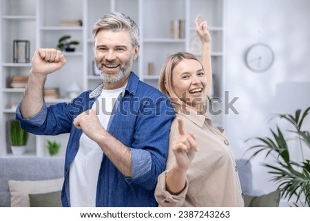 Happy senior couple dancing in their cozy living room, smiling looking at camera, happy long marriage, husband and wife spending weekend at home. Royalty-Free Stock Photo #2387243263