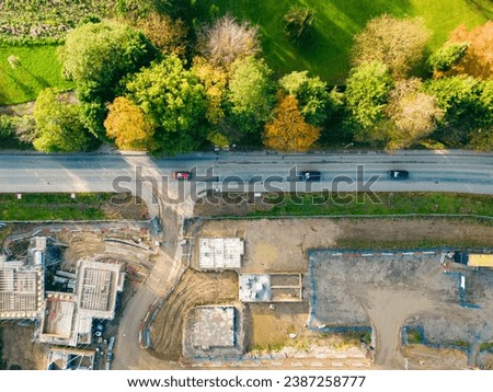 Drone top down view of a the entrance to a controversial housing development in the UK. A busy road bypass can be seen adjacent to autumn trees.
