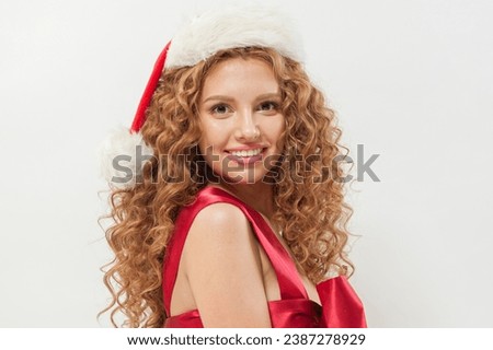 Attractive young woman in Santa hat posing. Beautiful female model with long wavy hair and cheerful smile on white background