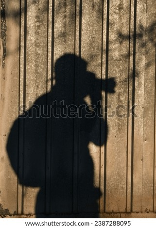 Photographers day concept. Portrait shadow of the man holding camera. On the metal tin wall. Sunset time.