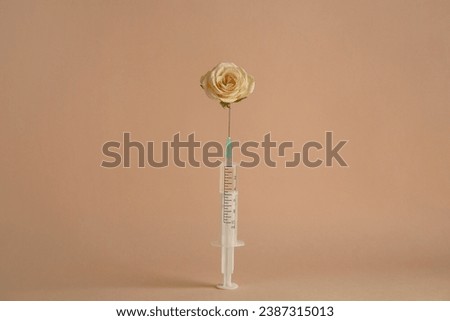 Medical syringe and rose flower on beige background Royalty-Free Stock Photo #2387315013