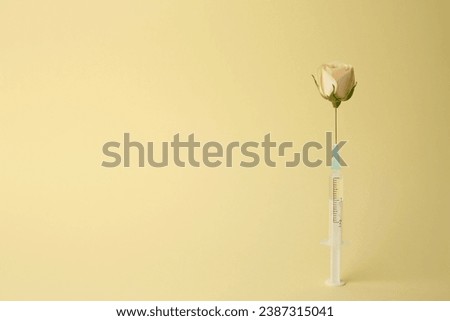 Medical syringe and rose flower on pale yellow background. Space for text