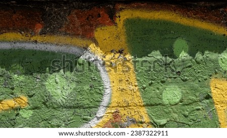Horizontal photo of an old concrete wall covered with dripped green and yellow paint, a dark shadow falling above.