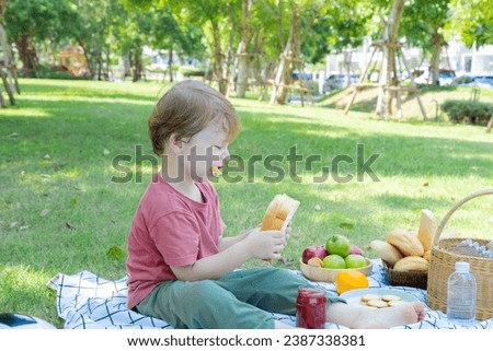 Happy little boy sitting in park having fun eating sandwich or bread with jam making by himself spending time picnic with mother in weekend summer holiday, Caucasian family relaxing vacation outdoors