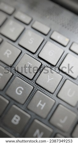 Close-up view of a sleek black laptop keyboard with prominent keys showing symbols and numbers on blurred dark surface
