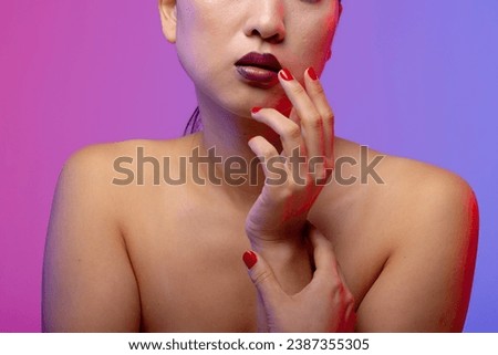 Asian woman wearing purple lipstick and red nail polish on purple background. Cosmetics, makeup, female fashion and beauty, unaltered.