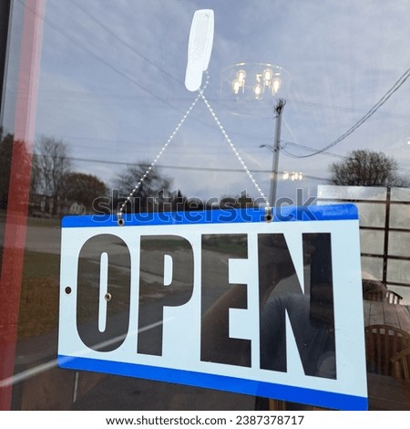 OpenClosed sign turned to open hanging in the window of a business with some reflection in the window. 