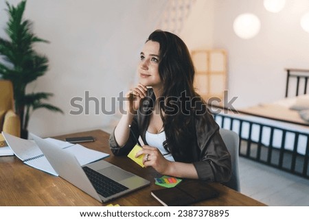 Smiling and thinking woman sitting at table in hostel room