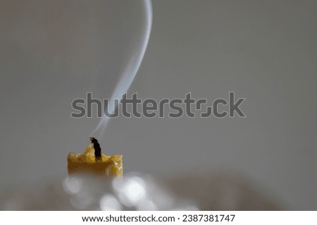 Serene and minimalist 
composition, a solitary beeswax candle with a faint tendril of smoke rises delicately from the extinguished wick, tracing an ephemeral path into the stillness of the air.