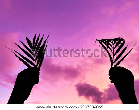 Lent Season,Holy Week, Palm Sunday and Good Friday concepts - Lent with silhouette of hands holding palm leaves in purple sky background. Stock photo.
