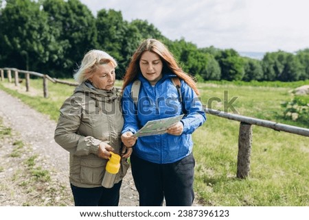Two happy Womans in active trekking clothes with map having a halt after hiking
