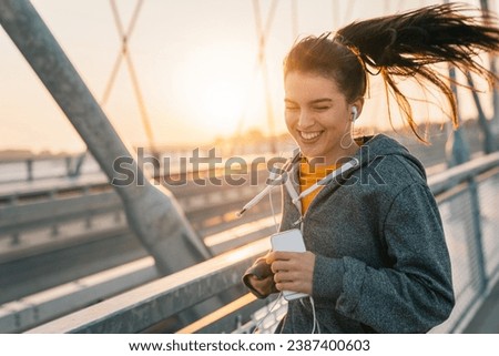 Attractive smiling woman promoting healthy lifestyle by jogging outdoors. Happy woman doing morning fitness routine while listening to music.