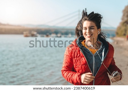 Waist up photo of beautiful young woman with long hair feeling joy and happiness while running on the beach with sea and bridge in the background.