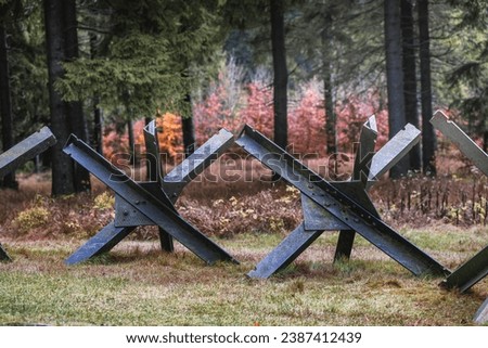 Old steel rusty anti tank roadblocks laid on grass with forest in the background on a gloomy dark day of winter without snow. Concept for war, defense, hard times.