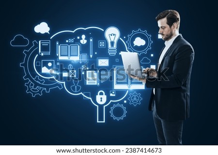 Attractive young european businessman using laptop with glowing brain outline and books hologram on blue background. Artificial intelligence, chat GPT, bot assistant and machine learning concept