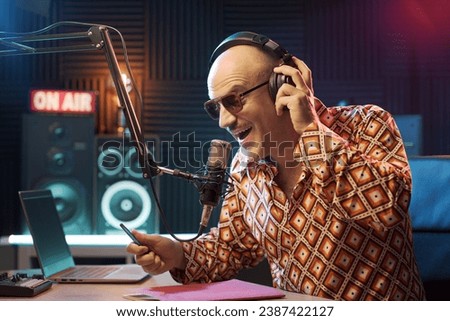 Host working at the radio broadcasting studio, he is talking into the microphone and wearing headphones