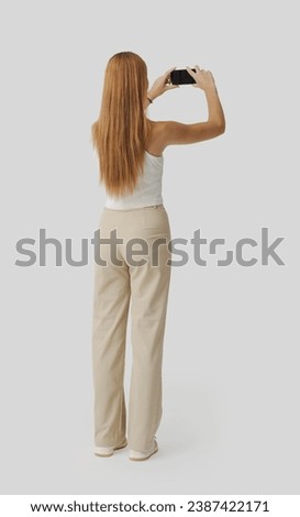 Young beautiful woman taking pictures with her smartphone and sharing online, back view