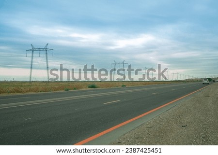 Electric transmission lines along the road in the steppe against the backdrop of the sunset blue sky. Horizontal photo