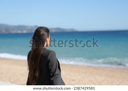 Single executive relaxing contemplating ocean sitting on the beach Royalty-Free Stock Photo #2387429581