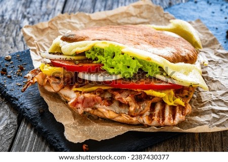 Big sandwich with grilled chicken breast and cheese and fresh vegetables on wooden table 
