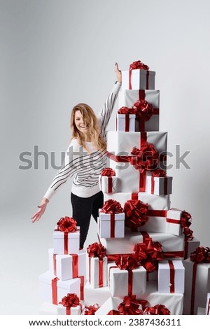A gorgeous beautiful young woman poses among a mountain of white gift boxes in a gray background. Beautifully decorated for Christmas. Holiday fashion. Sales and shopping.