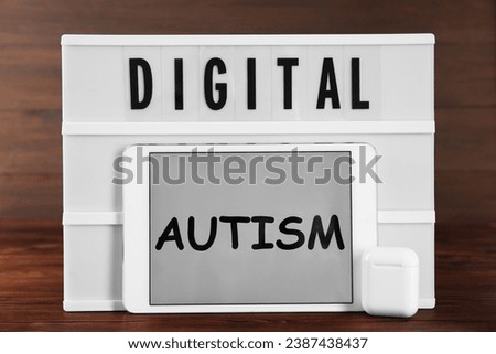 Lightbox, tablet with words Digital Autism and earphones on wooden table. Addictive behavior