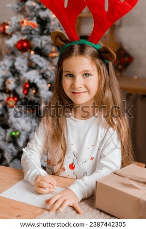 a cute little girl with long blond hair in New Year's pajamas at home writes a letter with wishes to Santa Claus. High quality photo